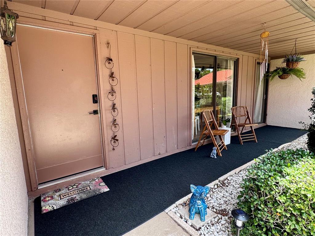 A covered porch features a tan front door, sliding glass doors, and two wooden chairs — 6378 DRAW LANE UNIT 36, SARASOTA, FL