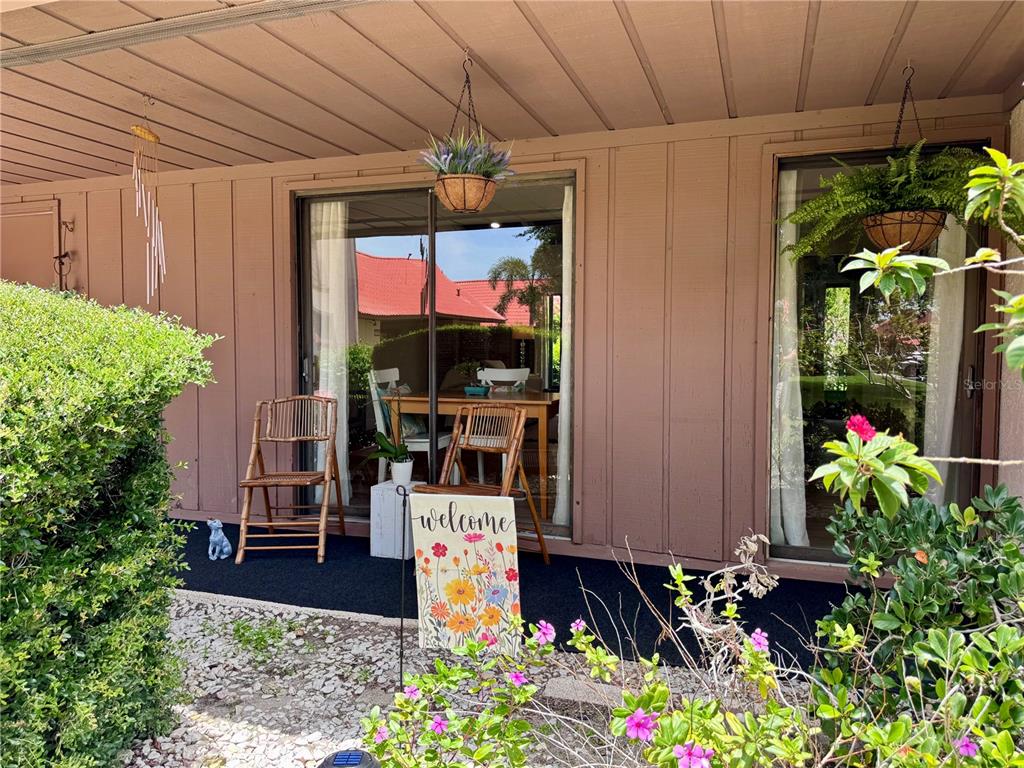 A patio with a sliding glass door, two bamboo chairs, and a floral welcome sign — 6378 DRAW LANE UNIT 36, SARASOTA, FL