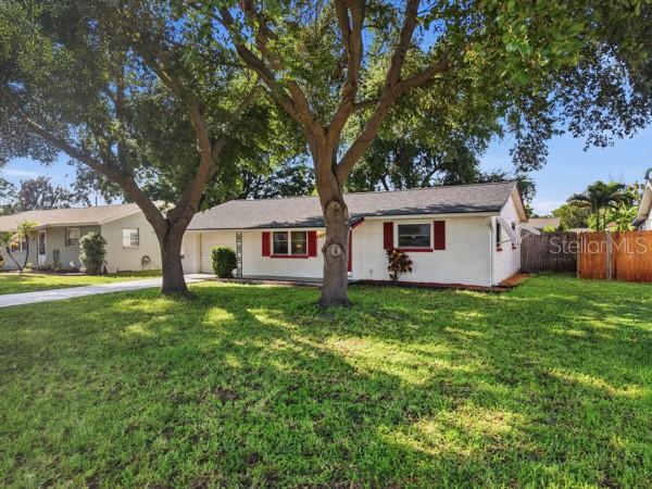 A white brick single-story house with red shutters sits behind large trees on a lawn — 5935 63RD AVENUE N, PINELLAS PARK, FL