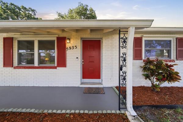 A white brick house exterior features a red front door, red shutters, and a gray porch — 5935 63RD AVENUE N, PINELLAS PARK, FL