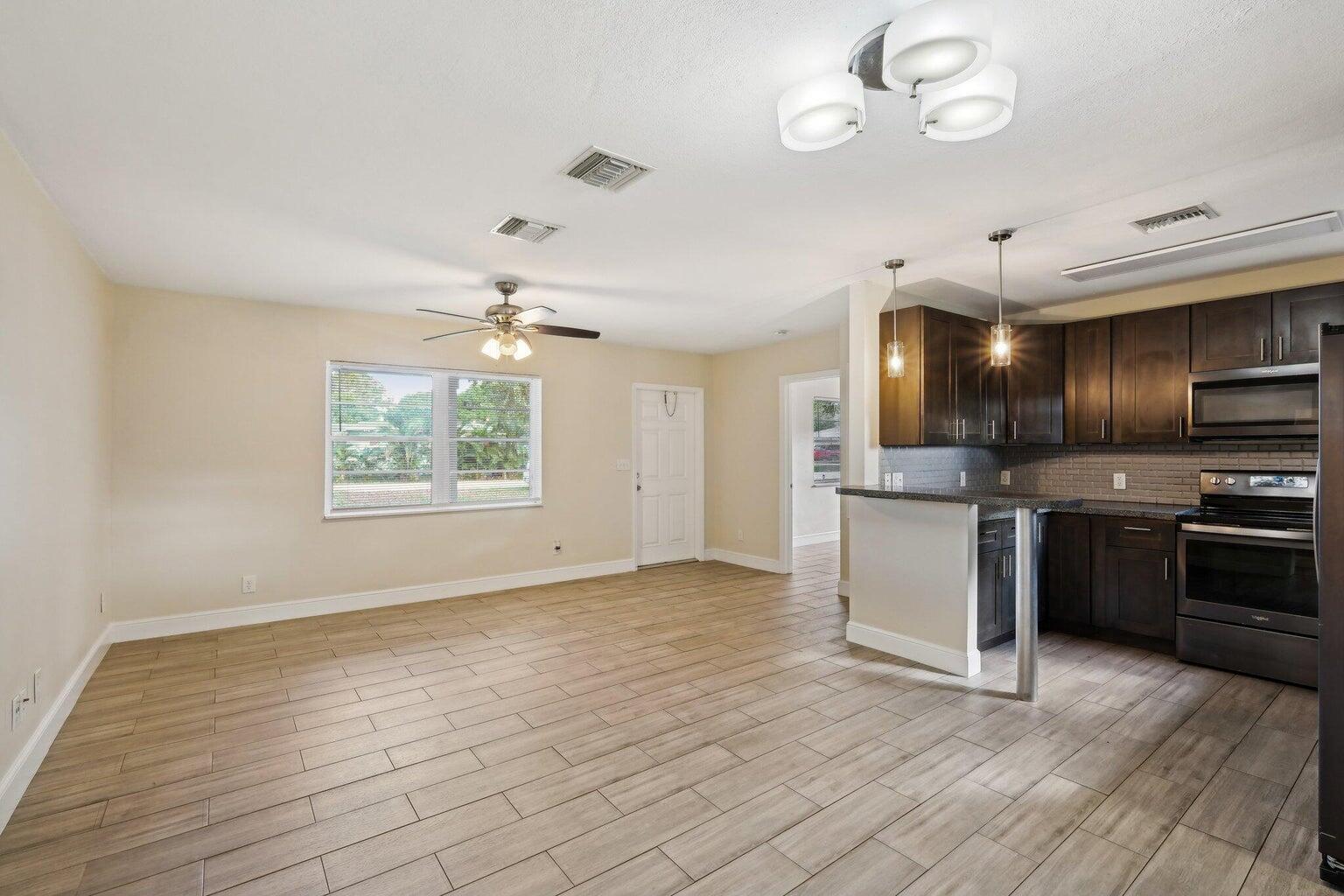 An open-concept kitchen and living area featuring dark wood cabinets and light wood-look tile flooring — 1455 15th Avenue, Vero Beach FL 32960, VERO BEACH, FL