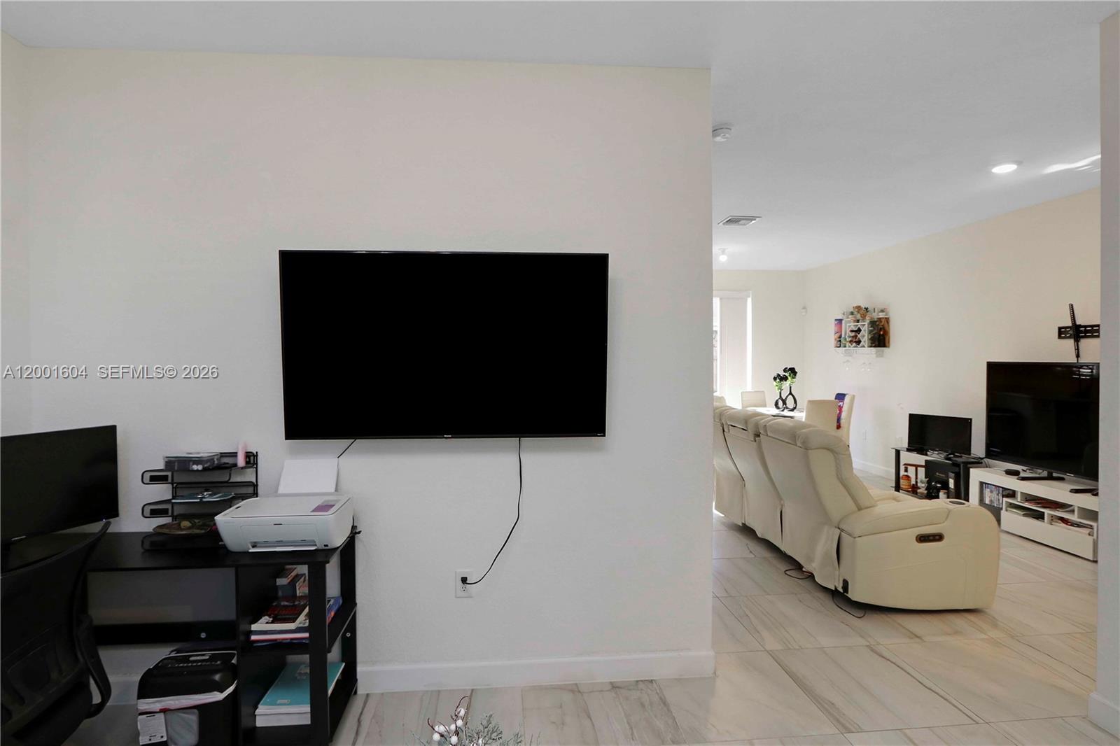 A wall-mounted television overlooks a desk area, with a living room visible beyond — 2432 SE 10th Ct, Homestead FL 33035, HOMESTEAD, FL