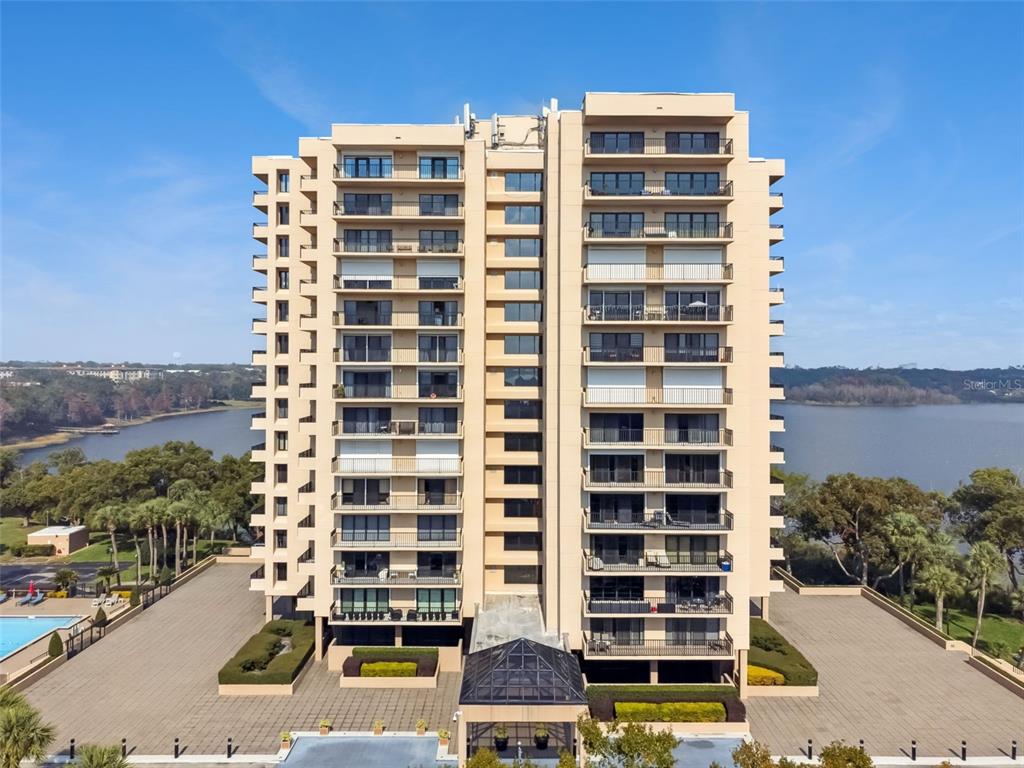 An aerial view of a tall, beige residential apartment building situated beside a lake — 7550 HINSON STREET UNIT 4b, ORLANDO, FL