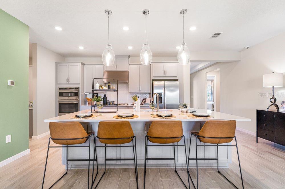 A kitchen features a large island with four bar stools, light cabinetry, and pendant lighting — 897 LADYFISH TRAIL, ST CLOUD, FL