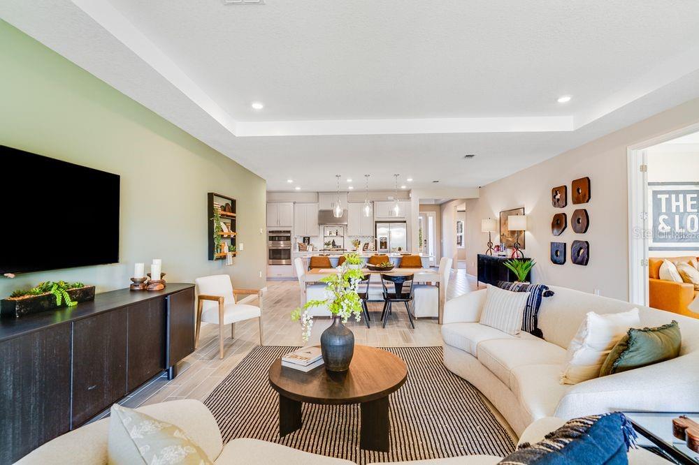 An open-concept living room and kitchen featuring light tile floors and a tray ceiling — 897 LADYFISH TRAIL, ST CLOUD, FL