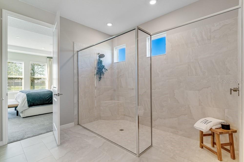 A modern bathroom features a large glass-enclosed walk-in shower with light-colored tile walls — 897 LADYFISH TRAIL, ST CLOUD, FL