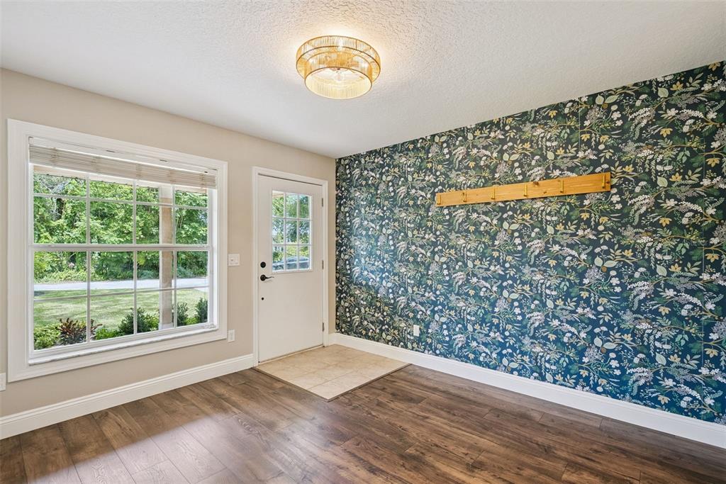 An entryway features wood-look flooring, a floral accent wall with a coat rack, and a window — 1459 AZALEA AVENUE, CASSELBERRY, FL