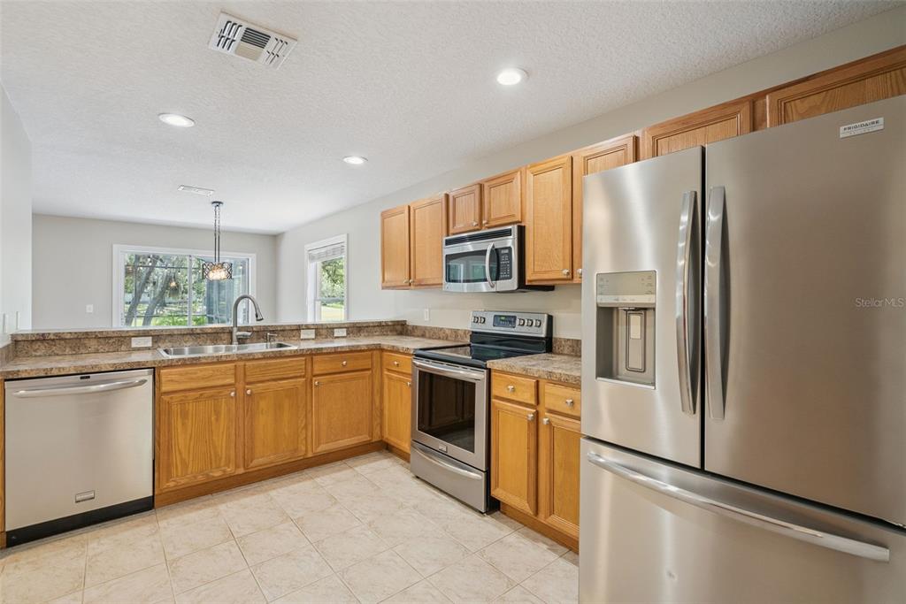 A kitchen features light wood cabinets, granite countertops, stainless steel appliances, and tile flooring — 1459 AZALEA AVENUE, CASSELBERRY, FL
