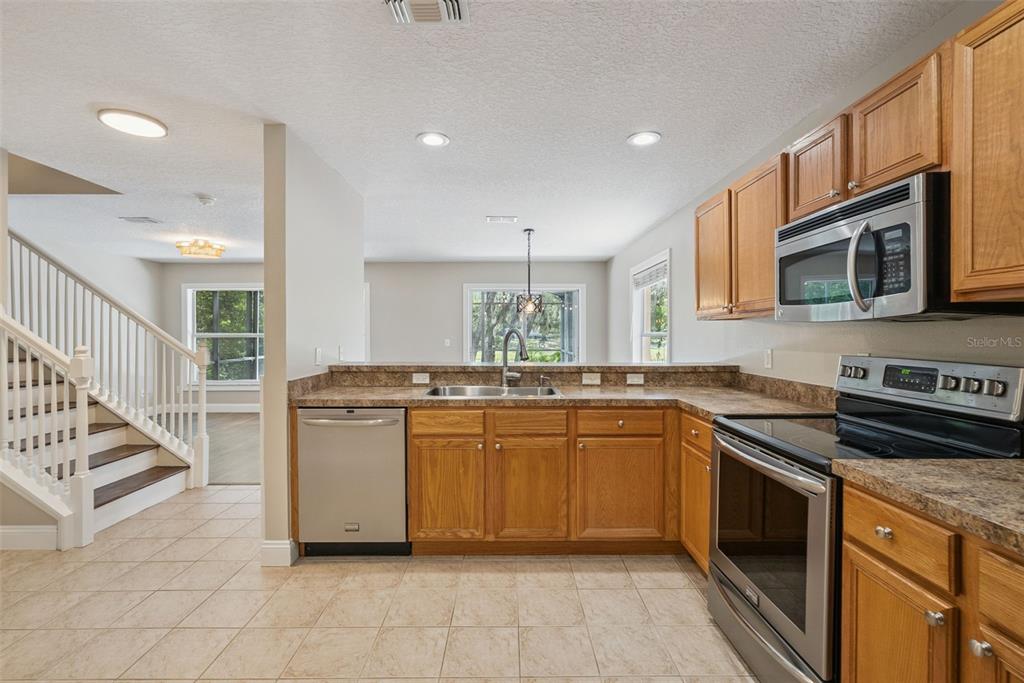 A kitchen with wood cabinets, stainless steel appliances, and tile flooring next to a staircase — 1459 AZALEA AVENUE, CASSELBERRY, FL