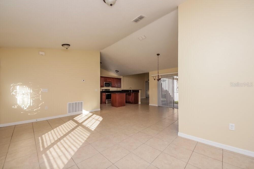 An open-concept living area features light-colored tile flooring and a view into the kitchen — 905 DERBYSHIRE DRIVE, KISSIMMEE, FL