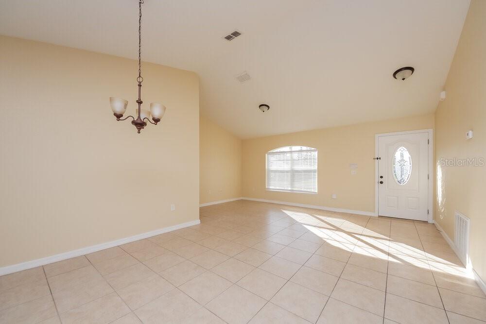 An empty room with beige walls, tile flooring, a chandelier, and a white front door — 905 DERBYSHIRE DRIVE, KISSIMMEE, FL