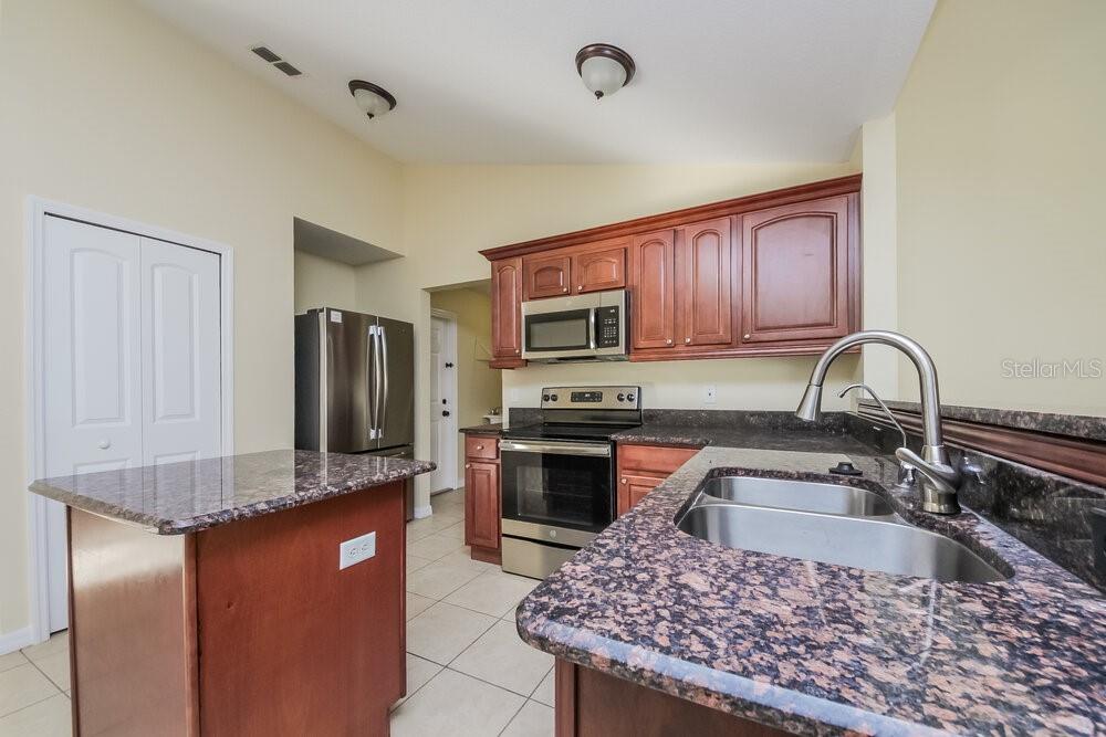 A kitchen with dark wood cabinets, granite countertops, stainless steel appliances, and a center island — 905 DERBYSHIRE DRIVE, KISSIMMEE, FL