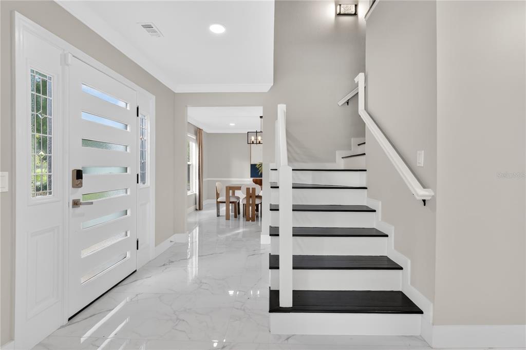 An entryway features white marble floors, a white front door, and a staircase with dark treads — 109 E 12TH AVENUE, WINDERMERE, FL