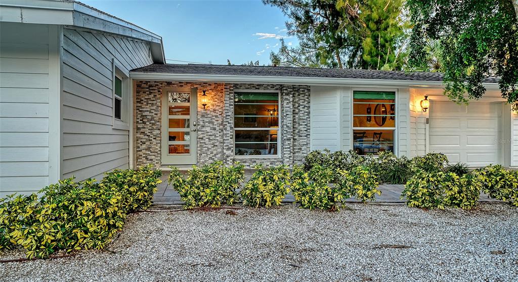 The exterior of a single-story house features light gray siding, stone veneer, and a gravel yard — 783 BIRDSONG LANE, SARASOTA, FL