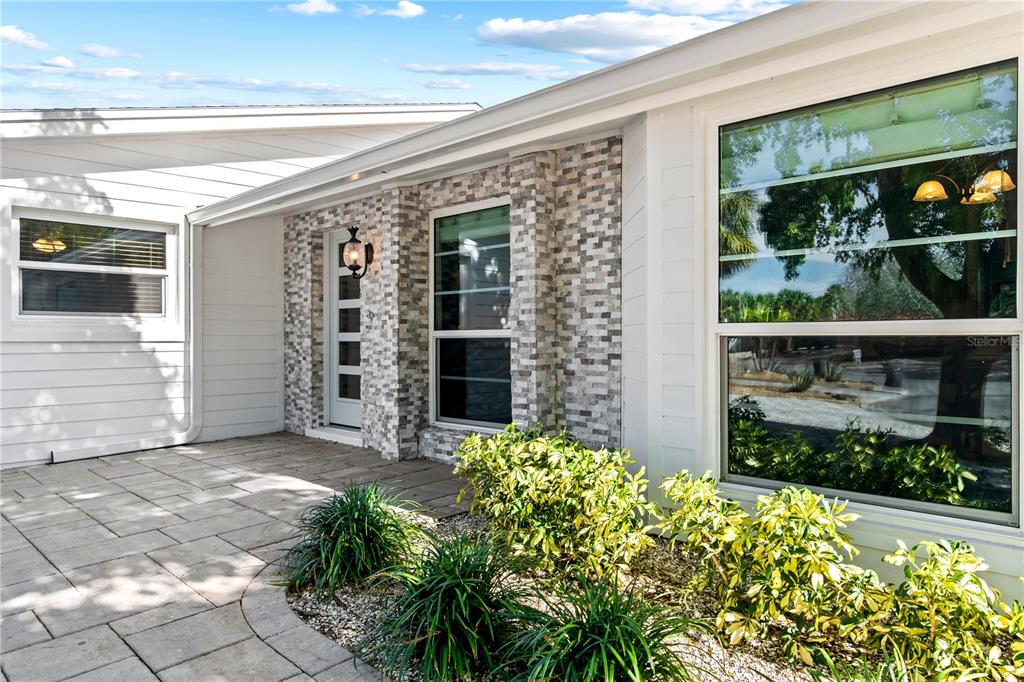 The exterior of a house features a stone-veneer entryway, white siding, and a paved patio — 783 BIRDSONG LANE, SARASOTA, FL