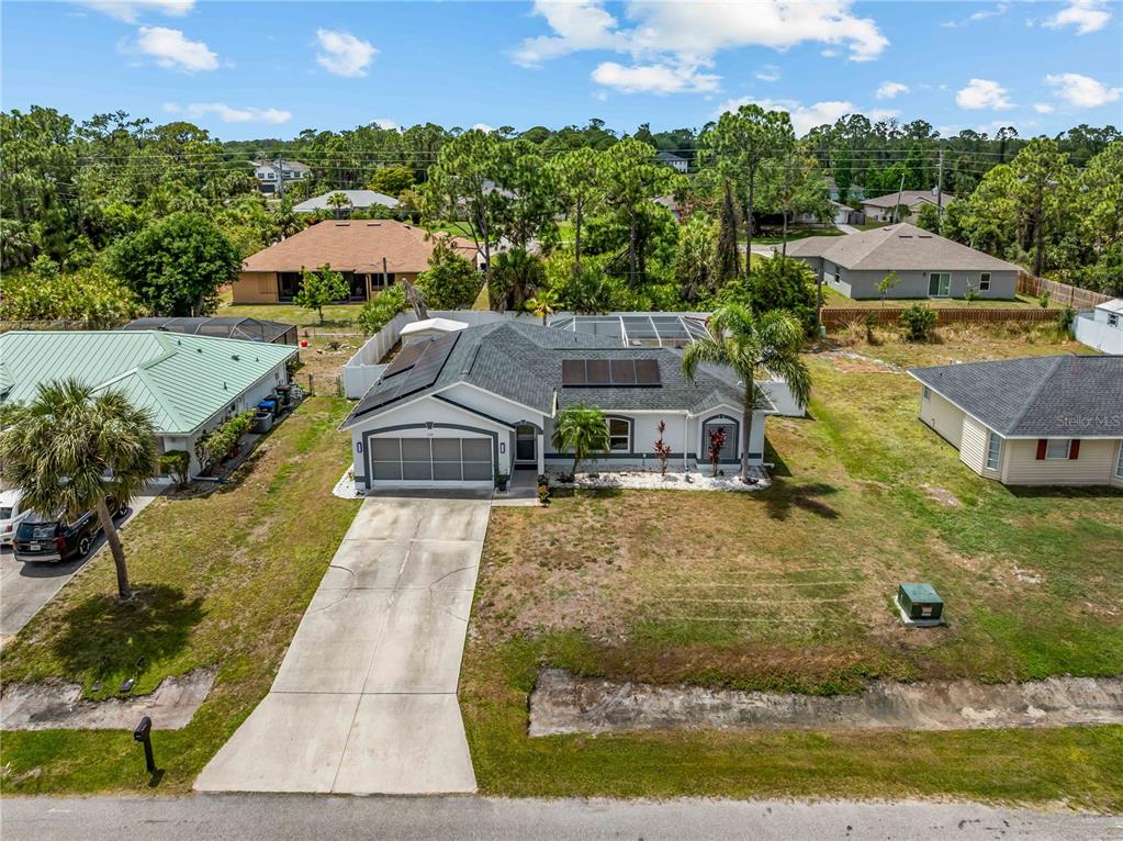 An aerial view shows a single-story house with a garage, solar panels, and a pool enclosure — 1729 MILAN STREET, NORTH PORT, FL