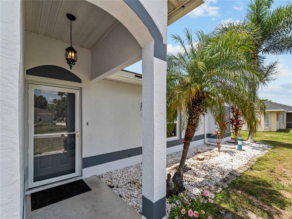 A covered entryway features a glass storm door, a hanging lantern, and a palm tree — 1729 MILAN STREET, NORTH PORT, FL