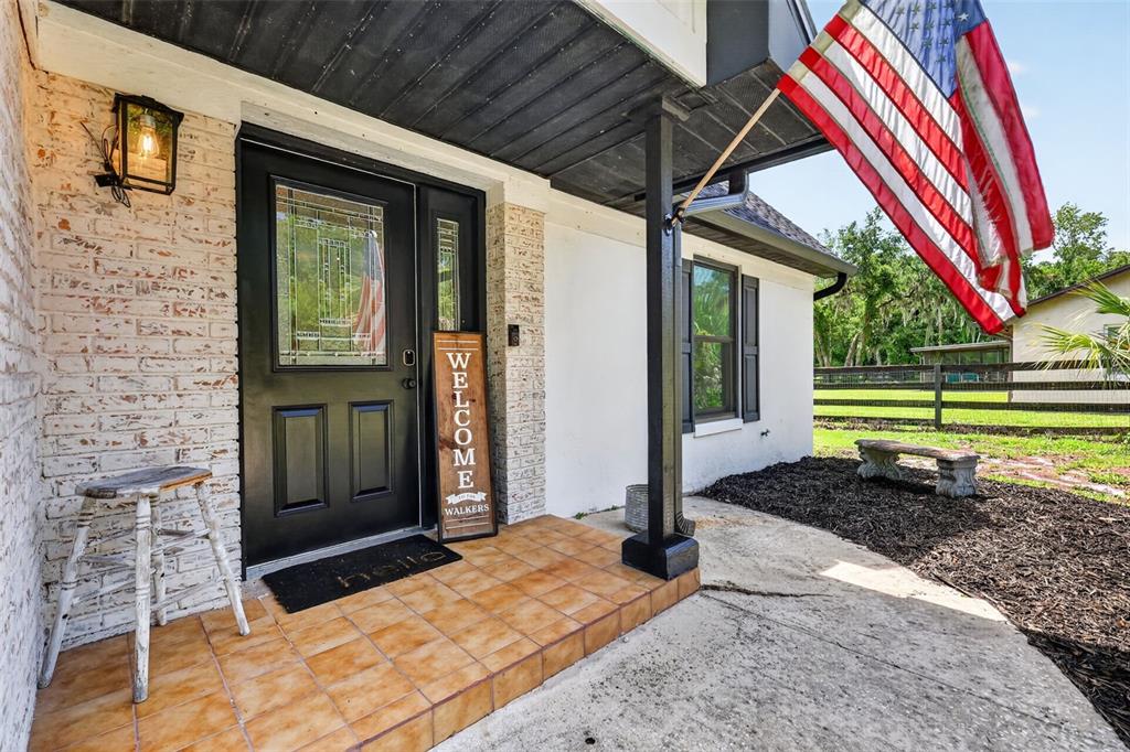 A front porch features a black door, a welcome sign, and an American flag — 32589 OKALOOSA TRAIL, SORRENTO, FL