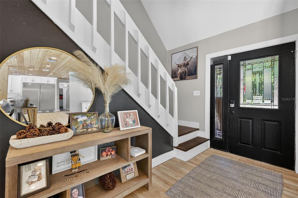 An entryway features a wooden console table, a round mirror, and stairs with white railings — 32589 OKALOOSA TRAIL, SORRENTO, FL