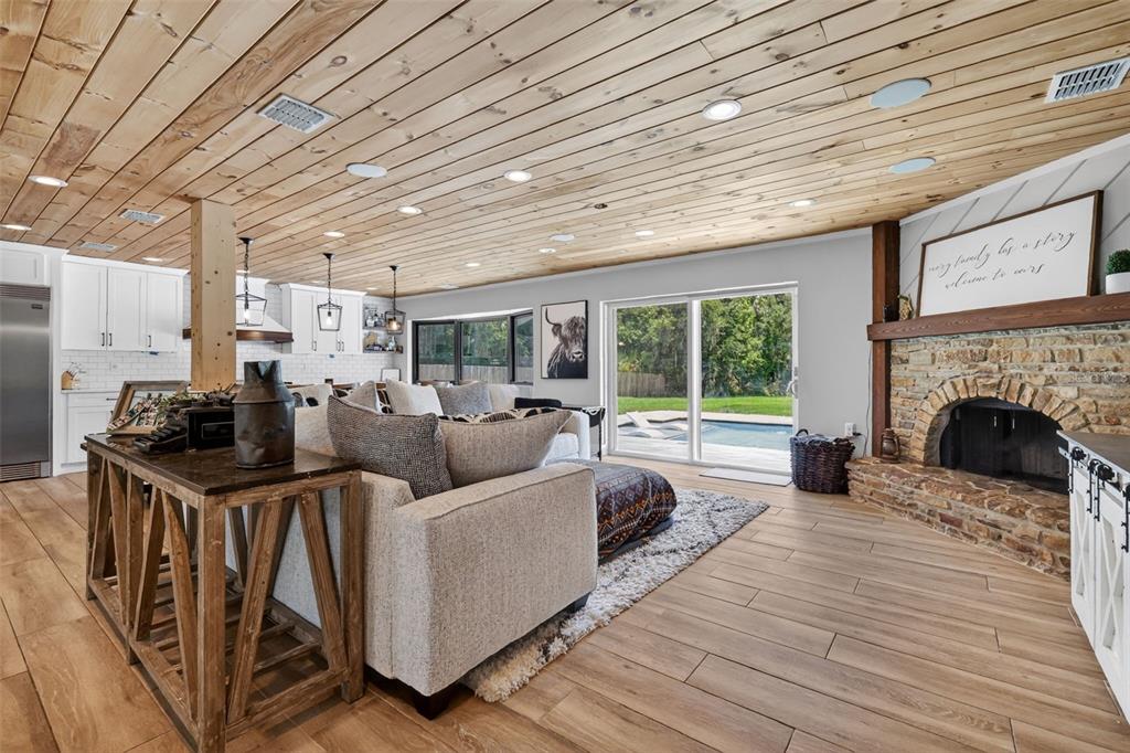 A living room with a wood-plank ceiling, stone fireplace, and sliding doors overlooking a pool — 32589 OKALOOSA TRAIL, SORRENTO, FL