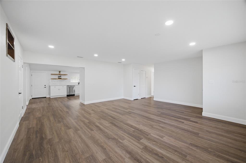 A spacious living area with light gray walls and wood-look flooring leads to a kitchen — 3502 LILES LANE, PLANT CITY, FL