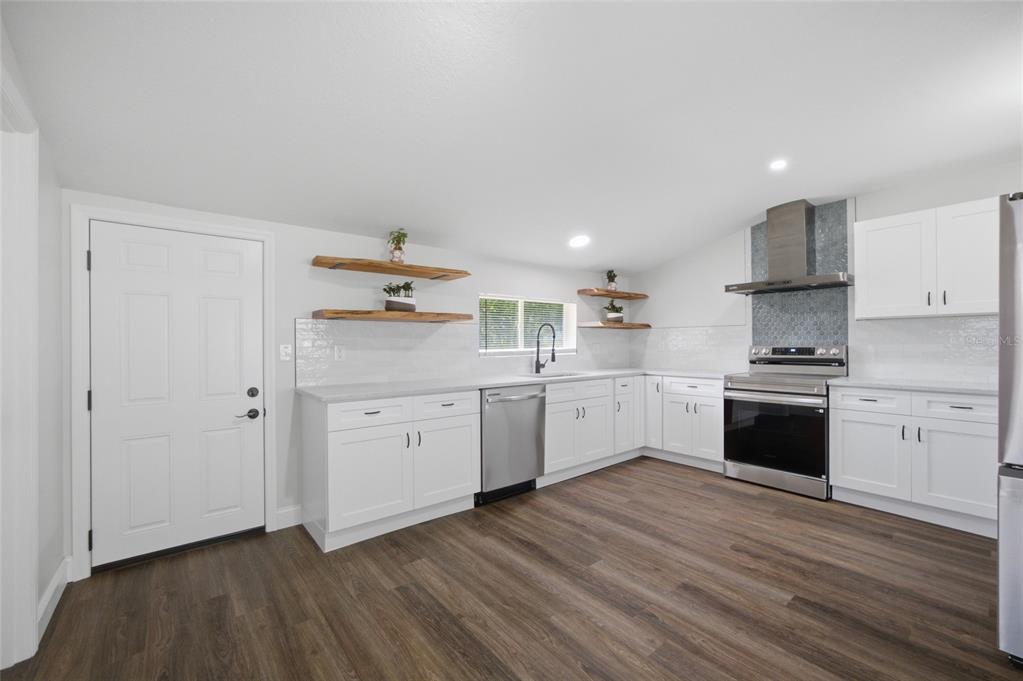 A bright kitchen features white cabinets, stainless steel appliances, wood floating shelves, and wood flooring — 3502 LILES LANE, PLANT CITY, FL