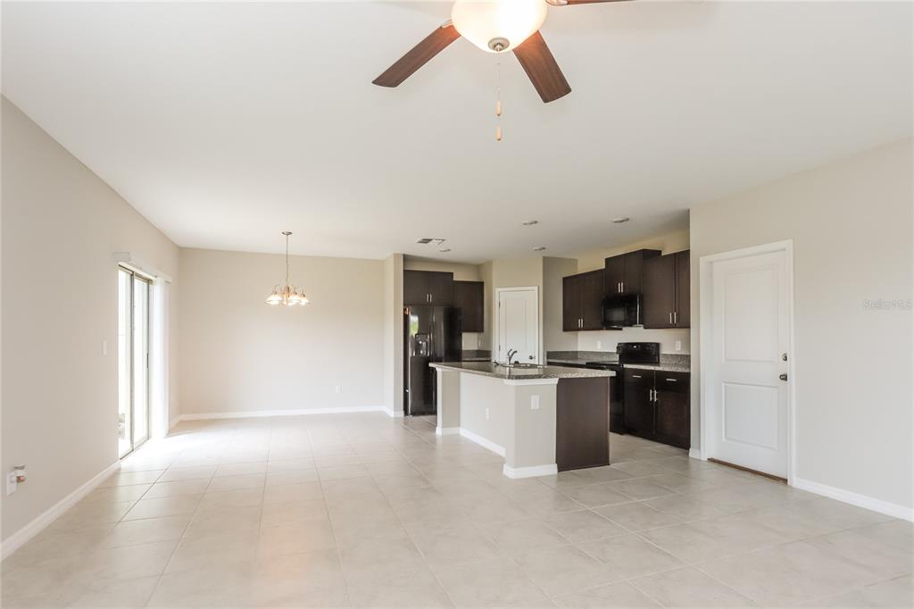An open-concept kitchen and dining area features dark wood cabinets, granite countertops, and tile flooring — 15519 WICKED STRONG STREET, SUN CITY CENTER, FL
