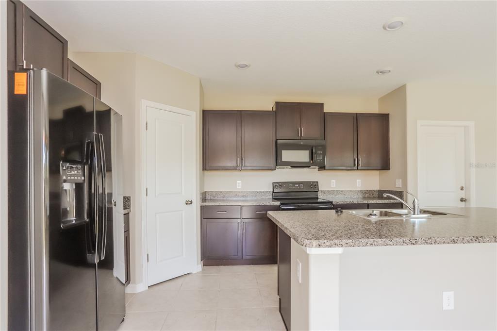 A kitchen features dark wood cabinets, granite countertops, a kitchen island, and black appliances — 15519 WICKED STRONG STREET, SUN CITY CENTER, FL
