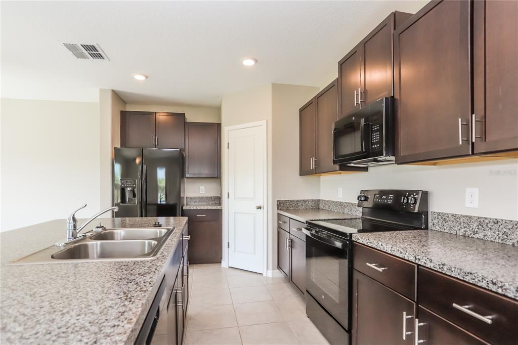 A kitchen features dark wood cabinets, granite countertops, stainless steel appliances, and tile flooring — 15519 WICKED STRONG STREET, SUN CITY CENTER, FL