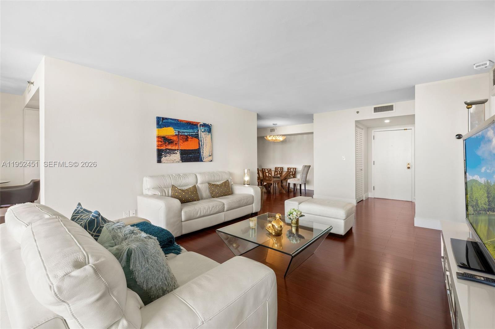 A living room features white leather sofas, a glass coffee table, and dark wood flooring — 4000 Towerside Ter # 2005, Miami FL 33138, MIAMI, FL