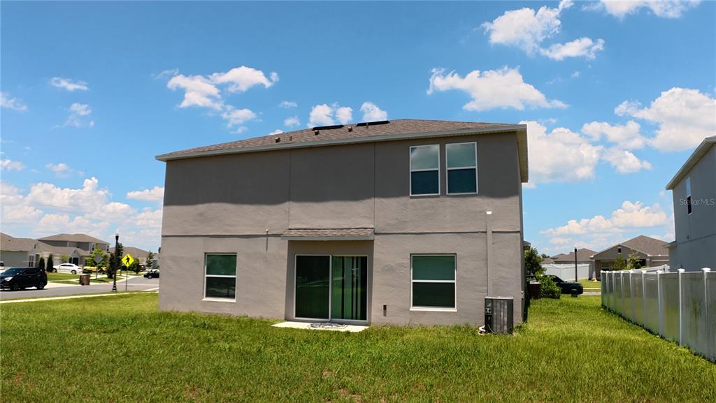 The exterior rear view of a two-story house features a sliding glass door and lawn — 282 AMBER WAY, KISSIMMEE, FL