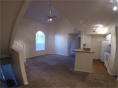 A living room with a vaulted ceiling and an adjacent kitchen with white appliances — 413 FOUNTAINHEAD CIRCLE UNIT 231, KISSIMMEE, FL