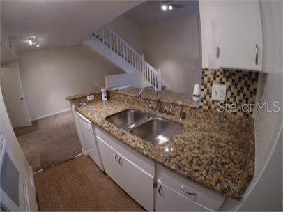 A kitchen with granite countertops and a double sink overlooks a carpeted living area — 413 FOUNTAINHEAD CIRCLE UNIT 231, KISSIMMEE, FL