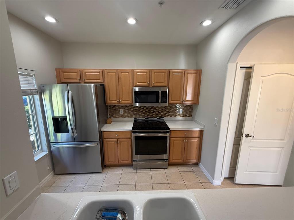 A kitchen features stainless steel appliances, wood cabinets, a tiled backsplash, and a double sink — 12985 COYOTE LN LANE, VENICE, FL
