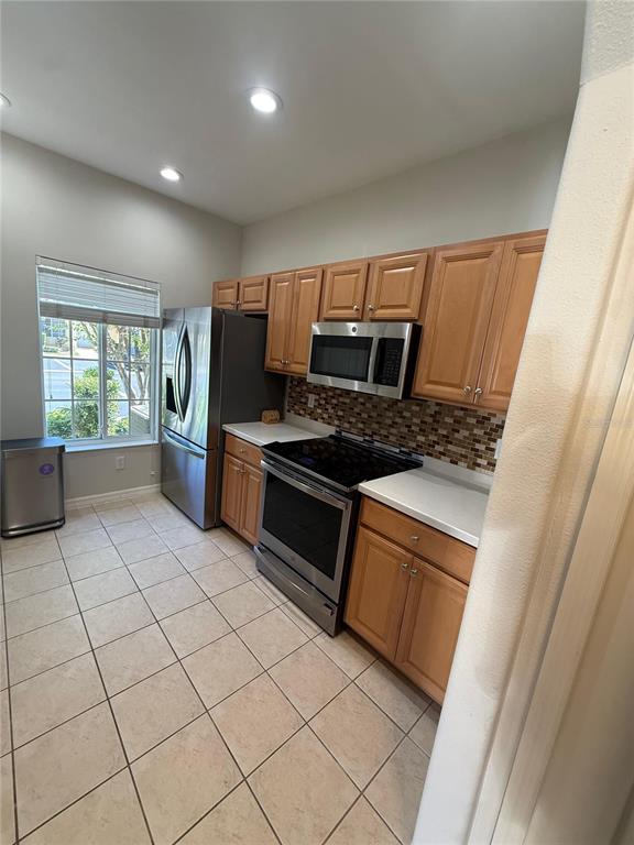 A kitchen features light wood cabinets, stainless steel appliances, a tiled backsplash, and tile flooring — 12985 COYOTE LN LANE, VENICE, FL