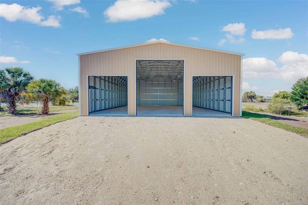 A tan metal building with three open garage bays sits on a gravel lot — 6041 GROVE BOULEVARD, PUNTA GORDA, FL