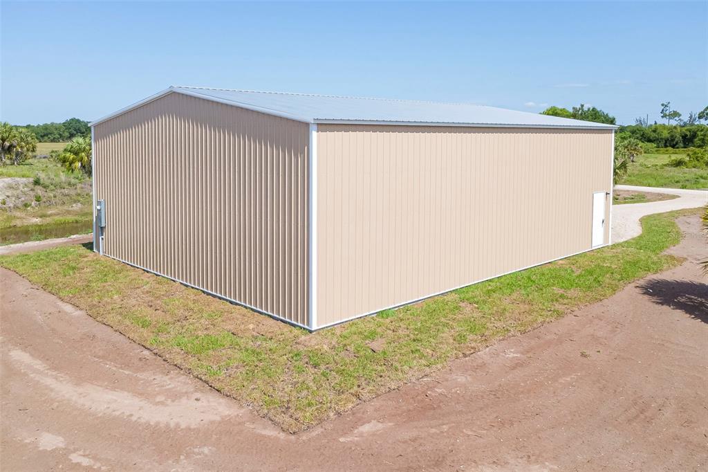 A tan metal storage building sits on a dirt lot under a clear blue sky — 6041 GROVE BOULEVARD, PUNTA GORDA, FL