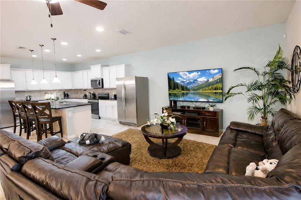 An open-concept living room and kitchen featuring a large sectional sofa and stainless steel appliances — 2147 TRIPOLI COURT, KISSIMMEE, FL