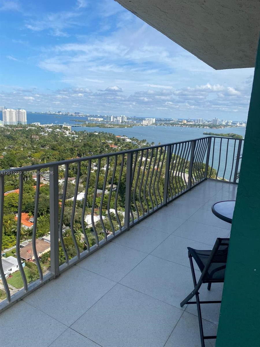 A balcony with a metal railing overlooks a bay, lush greenery, and a distant city skyline — 780 NE 69th St # 1210, Miami FL 33138, MIAMI, FL