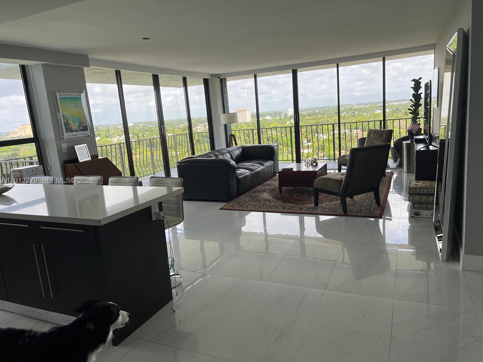 A modern living room with white tile floors, floor-to-ceiling windows, and a balcony view — 780 NE 69th St # 1210, Miami FL 33138, MIAMI, FL