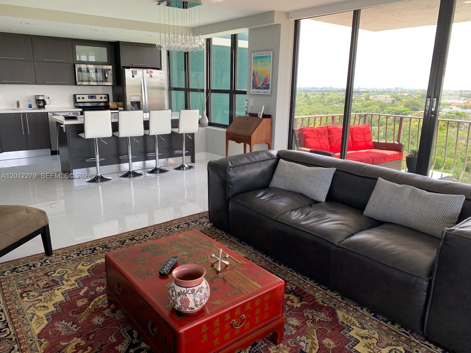 An open-plan living room and kitchen with a balcony, dark cabinetry, and a red coffee table — 780 NE 69th St # 1210, Miami FL 33138, MIAMI, FL
