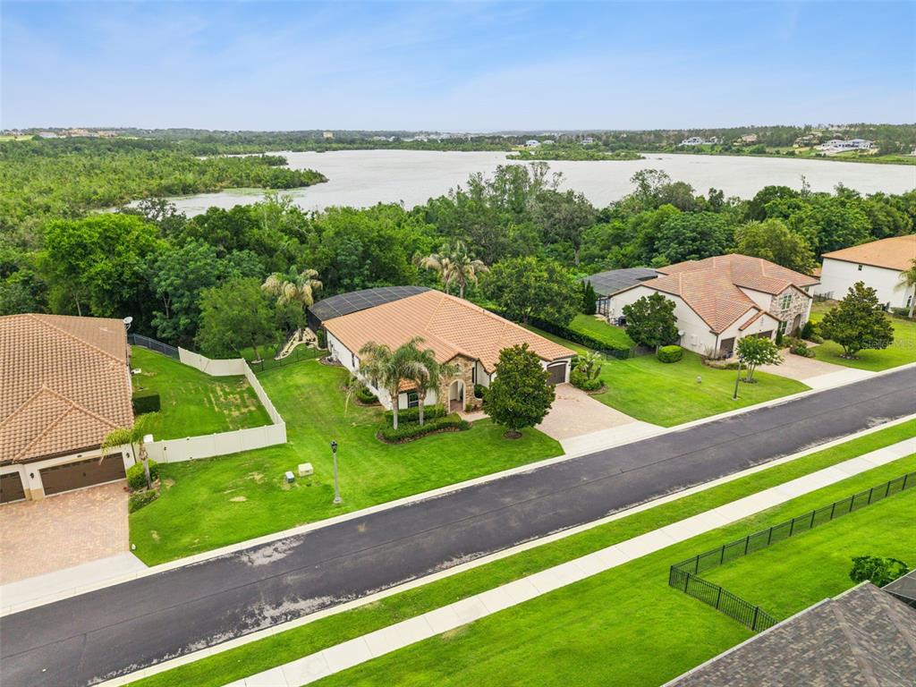 An aerial view shows suburban houses with tile roofs near a lake and trees — 16704 CARAVAGGIO LOOP, MONTVERDE, FL
