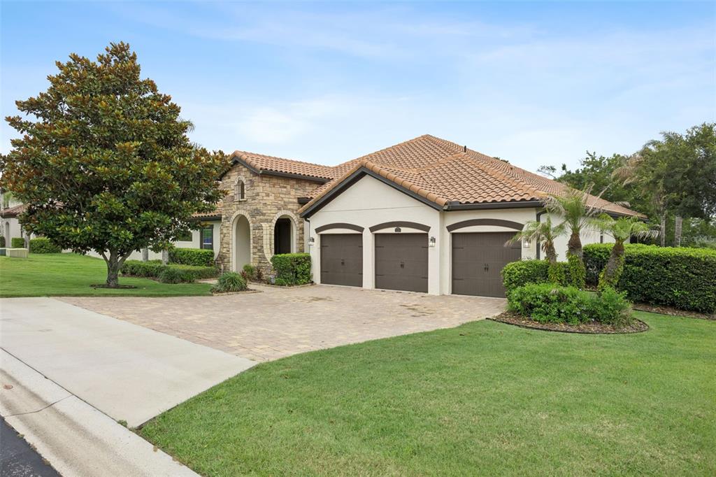 A single-story house with a stone facade, three-car garage, and a tiled roof — 16704 CARAVAGGIO LOOP, MONTVERDE, FL