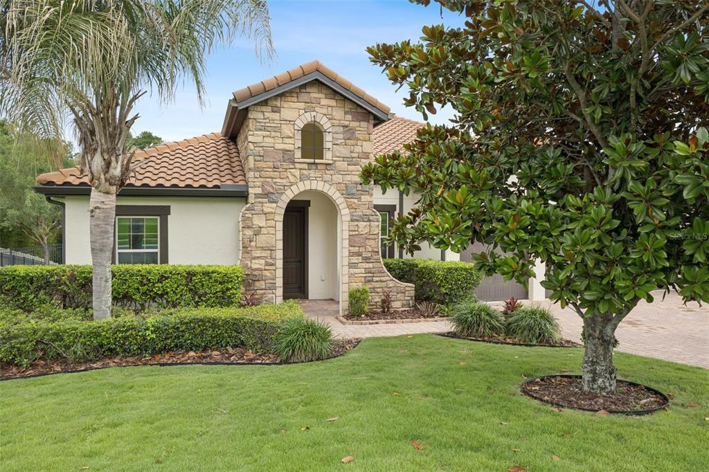 A single-story house with a stone-accented entryway, tiled roof, and a manicured front lawn — 16704 CARAVAGGIO LOOP, MONTVERDE, FL