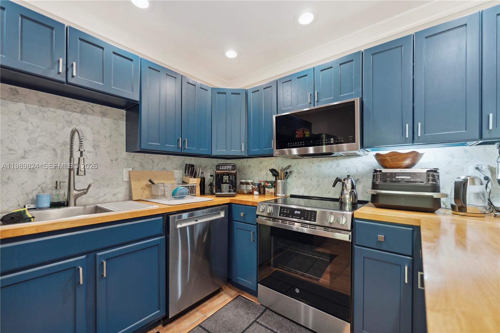 A kitchen features blue cabinets, butcher block countertops, stainless steel appliances, and marble-patterned backsplash tiles — 1111 SW 5th St, Boca Raton FL 33486, BOCA RATON, FL