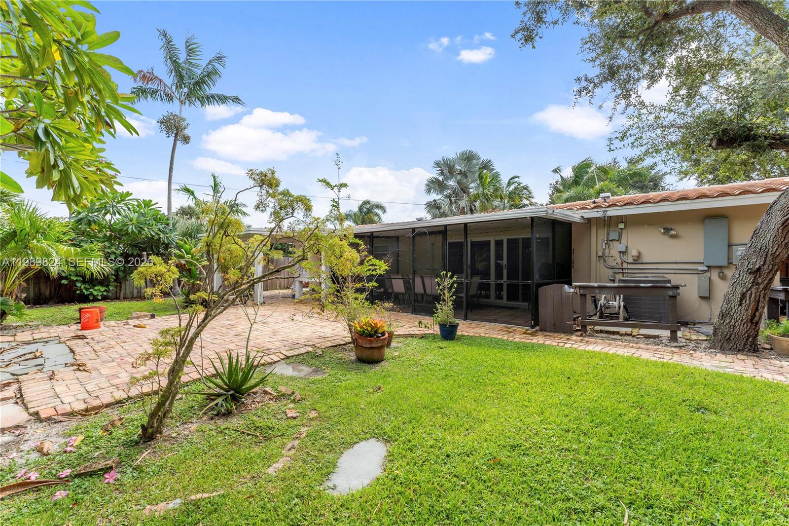 A backyard features a brick patio, a screened-in porch, and lush tropical landscaping — 1111 SW 5th St, Boca Raton FL 33486, BOCA RATON, FL