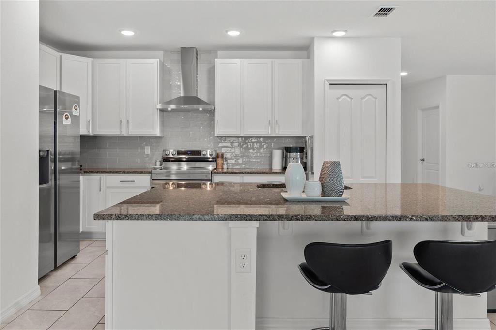 A modern kitchen features white cabinets, granite countertops, a stainless steel range, and a breakfast island — 923 FIELDSTONE WAY, HAINES CITY, FL