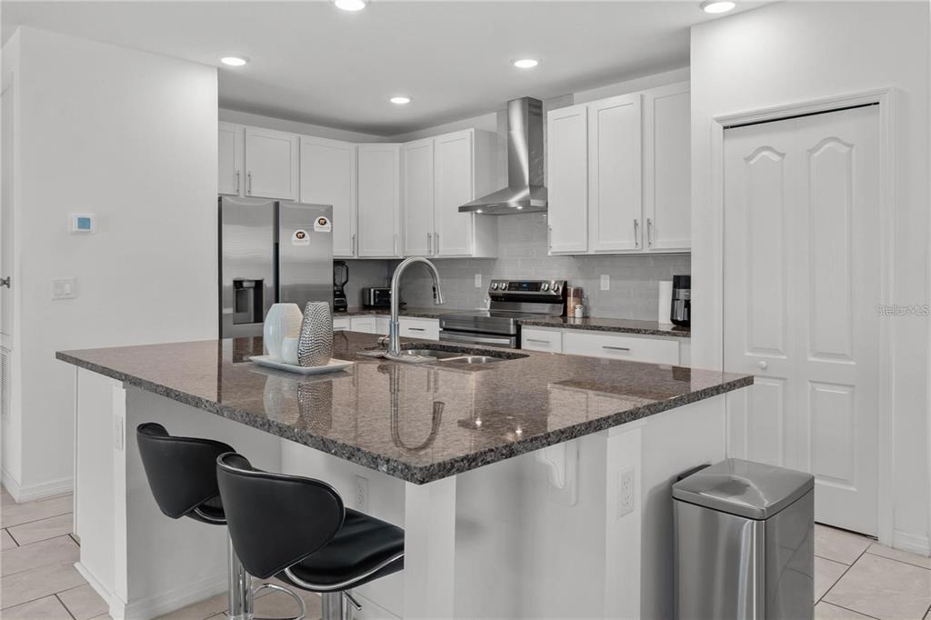 A kitchen features white cabinets, granite countertops, a center island with seating, and stainless appliances — 923 FIELDSTONE WAY, HAINES CITY, FL