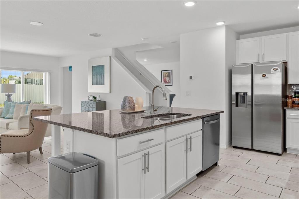 A kitchen island with a granite countertop sits in front of a stainless steel refrigerator — 923 FIELDSTONE WAY, HAINES CITY, FL