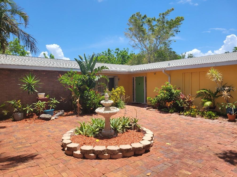 A brick courtyard features a central tiered fountain surrounded by lush landscaping and a house — 315 S TESSIER DRIVE, ST PETE BEACH, FL
